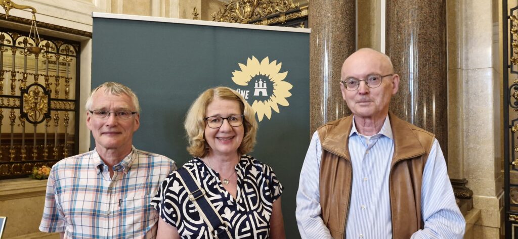 Die PER-Mitglieder Frau Karen Dabels, Herr Jochen Hartmann und Herr Manfred Knüppel vor einer Stellwand der Grünen Bürgerschaftsfraktion.